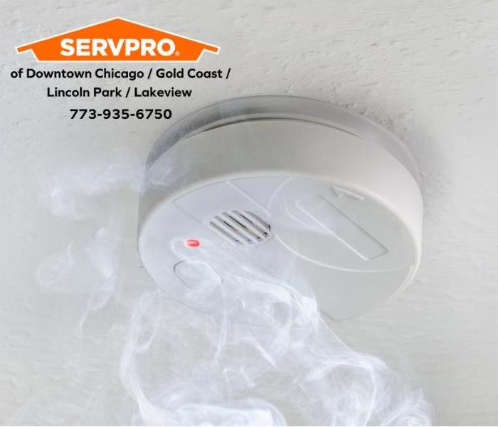 White smoke alarm with smoke on a white ceiling.